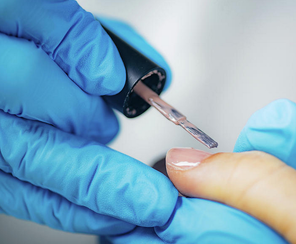 Manicurist applying a clear coat on finger nails