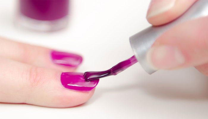 Manicurist painting a finger nails in red purple polish