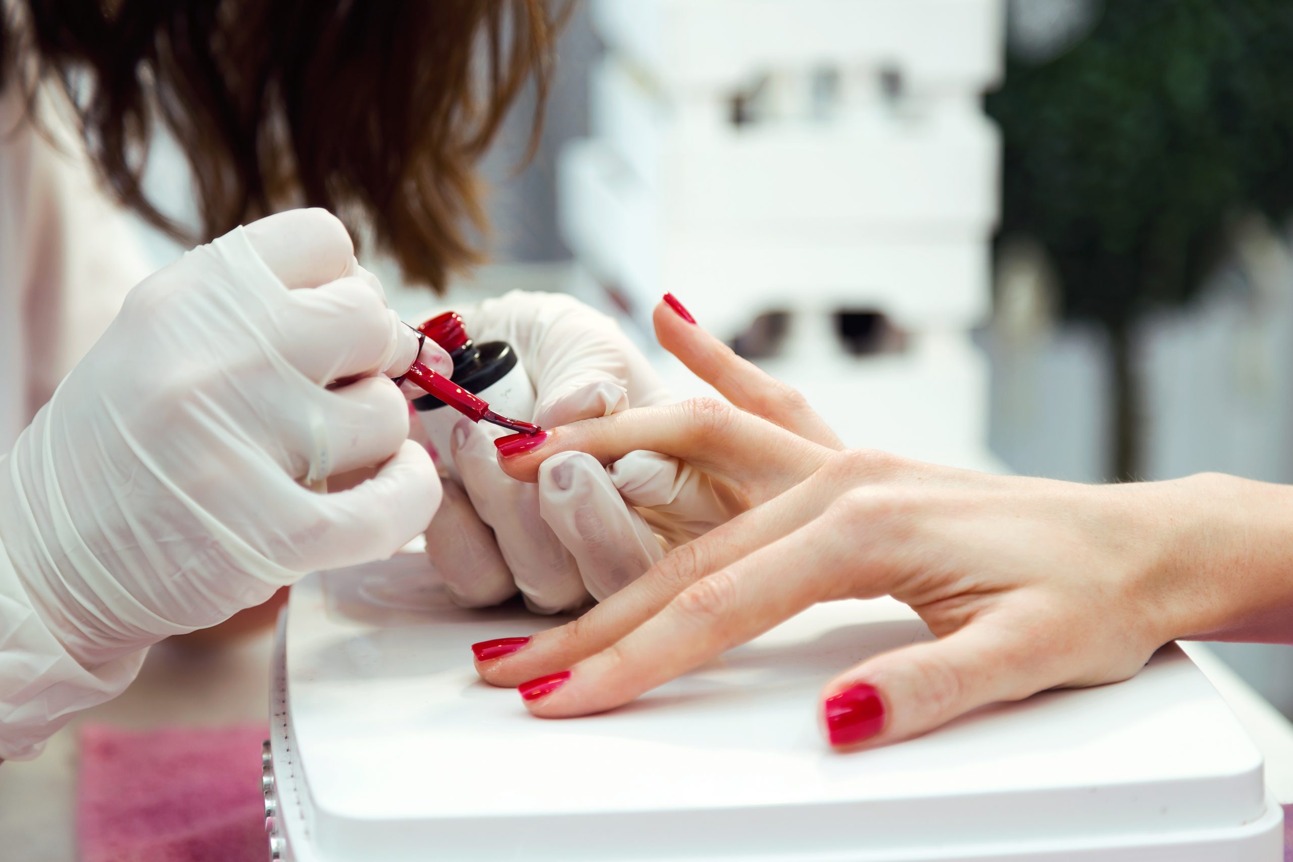 Nail technician painting finger hand with red polish